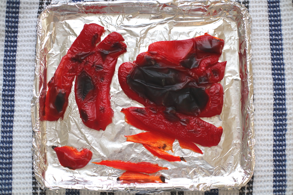 charred red bell peppers sliced and laid flat on baking sheet with aluminum foil on cloth