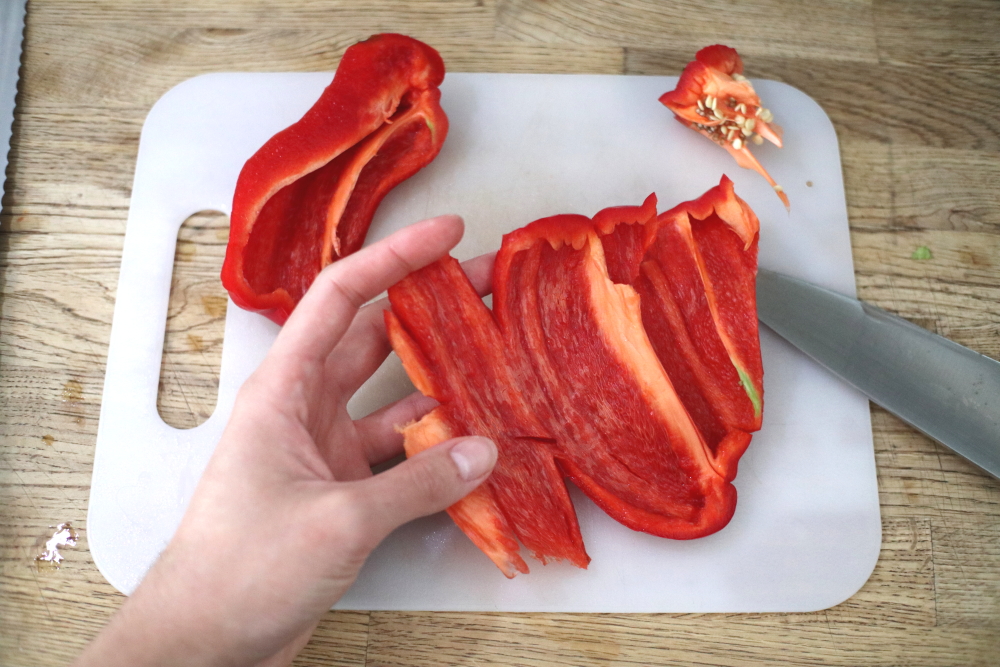 sliced red bell peppers on white cutting board on wooden counter with knife