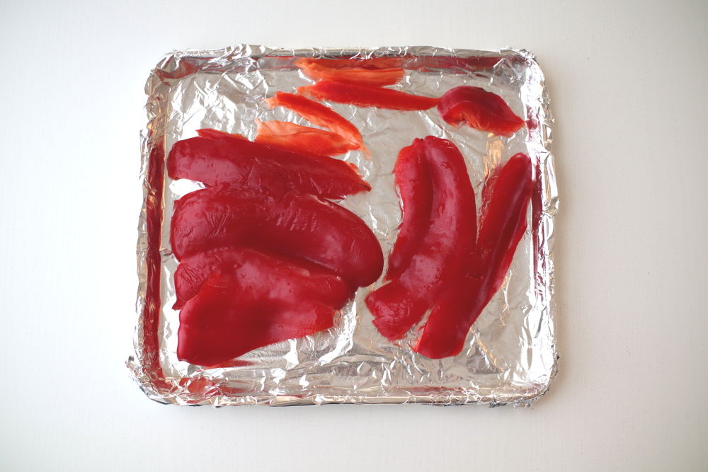 raw red bell peppers sliced and laid flat on baking sheet with aluminum foil on white table