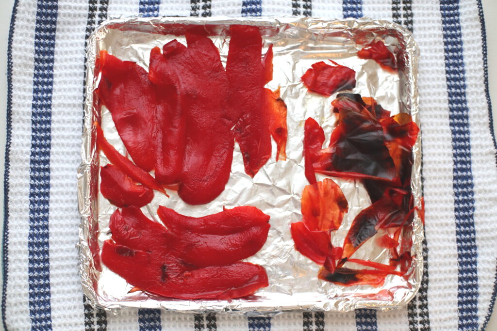 red bell peppers sliced and laid flat on baking sheet with aluminum foil on cloth char skin peeled