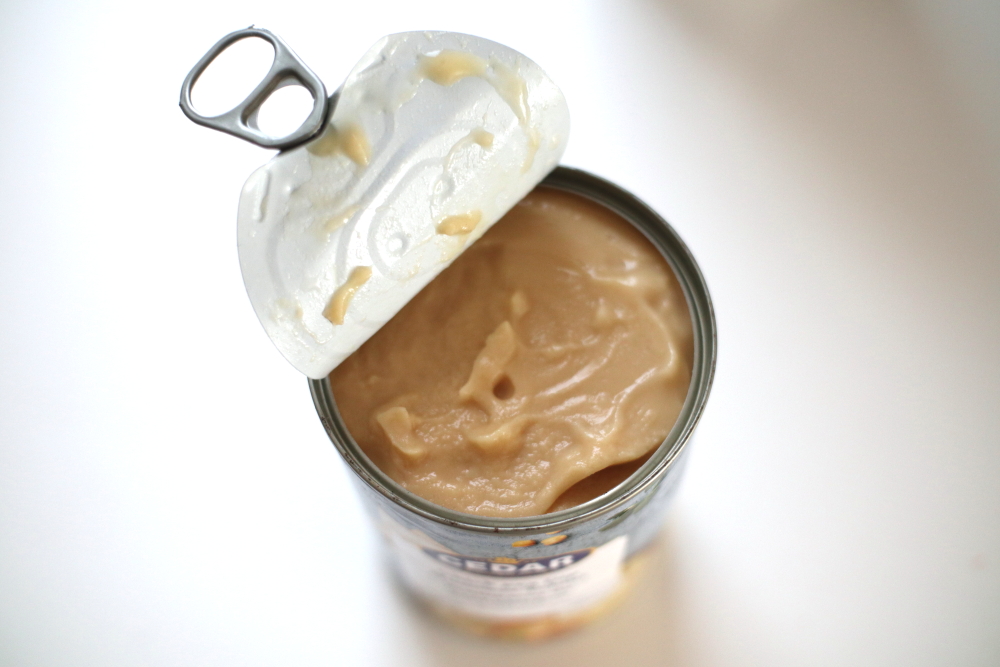 Canned hummus opened top view on white table bright background