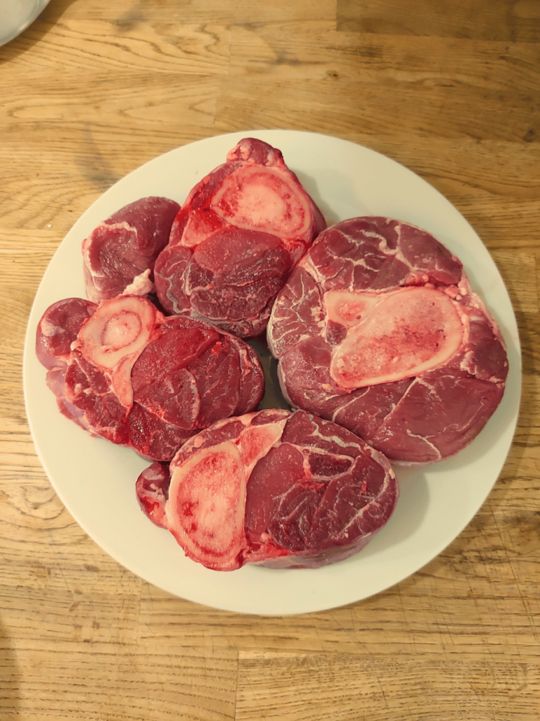 raw veal shank cross cuts top view on white plate on wood countertop